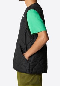Black quilted vest with side pockets, featuring a round neckline. Worn over a green short-sleeve shirt, displaying a smooth texture.