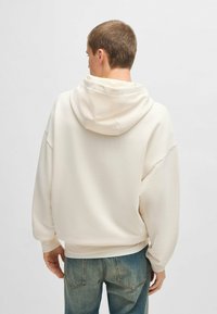 Felpa a capuccio di colore crema con una vestibilità comoda, spalle scese e una texture liscia. Abbinata a jeans azzurri chiari.