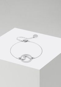 Braccialetto d'argento con pendente circolare decorato da un design a onda, collegato da una delicata catena con chiusura regolabile e prolungamento.