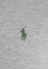 Joueur de polo vert brodé à cheval tenant un maillet levé, cousu sur un tissu tricoté gris clair.