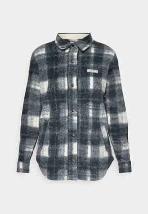 Plaid flannel shirt in black, white, and gray tones. Features a button-up front, collar, side pockets, and a logo patch on the chest.