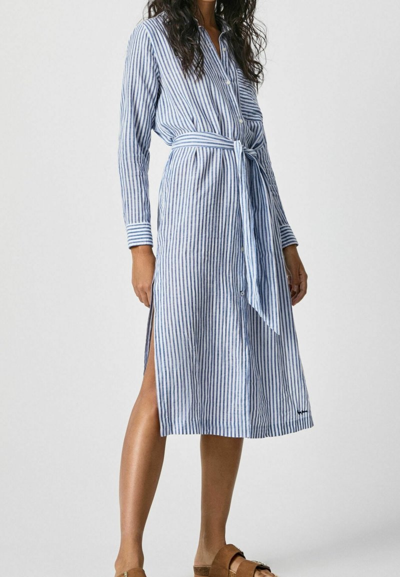 Robe chemise à rayures bleues et blanches avec manches longues, boutonnée sur le devant et ceinture à la taille. Dotée de fentes sur les côtés et d'une coupe mi-longue jusqu'aux genoux.
