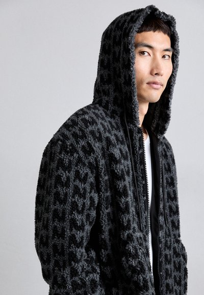 Black fleece zip-up hoodie with textured, raised design; features a hood, front zipper, and two side pockets. Soft and cozy material.