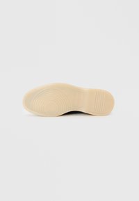 Svart skosåle med en glatt beige gummiyttersåle som har konsentriske sirkulære mønstre og horisontale riller for grep.