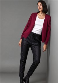 Burgundy knitted cardigan over a white top, paired with black faux leather joggers and ankle boots, set against a gray background.