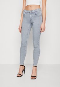 Jeans skinny gris claro con cuatro bolsillos, cierre de botón y detalles de costura sutiles. El material tiene una textura suave y elástica.