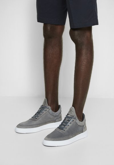 Grå semskede joggesko med teksturerte detaljer og hvite gummisåler. Har flate lisser og polstret krage. Båret sammen med mørke shorts.