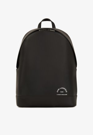 Sac à dos noir en matériau lisse et durable avec un haut arrondi, fermeture éclair et détail de marque blanc en bas.