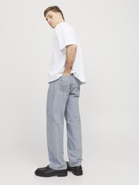 Camiseta blanca de gran tamaño, jeans de mezclilla azul claro y zapatos negros de suela gruesa. Los jeans presentan un corte clásico y una textura desgastada.