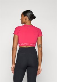 Tett rosa cropped sports topp med korte ermer og hvit Nike-logo. Har et bånd med "PRO" i en lysere rosa nyanse.