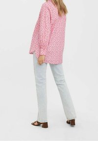 Pink long-sleeve shirt with a floral pattern, paired with light-wash straight-leg jeans and brown strappy sandals.