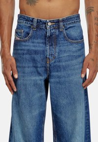 Jean en denim bleu avec une coupe droite, fermeture à bouton et poches avant. Présente des coutures visibles et une légère décoloration.