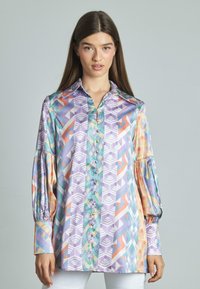 Camicia di seta multicolore con motivi geometrici in viola, turchese e corallo, maniche lunghe a sbuffo, colletto e chiusura frontale con bottoni.