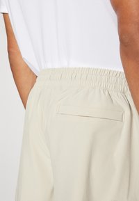 Ljust beige elastiska shorts med bakficka, med mjukt tyg och minimalistisk design. Midjan har rynkade detaljer.