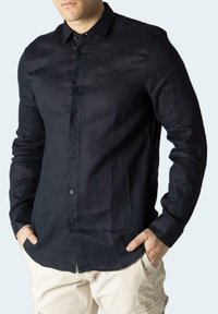 Camicia a maniche lunghe blu scuro realizzata in tessuto leggero con chiusura a bottoni, presenta un logo discreto sul petto e una vestibilità regolare.
