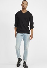 Black v-neck sweater with long sleeves, paired with light blue jeans rolled at the cuffs, and black ankle boots.