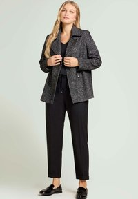 Manteau à motif chevrons noir et blanc avec un col cranté, des boutons doubles et une coupe décontractée, associé à un pantalon noir et des chaussures noires.