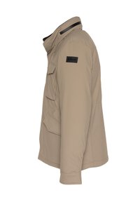 Giacca beige con chiusura a zip, tasche applicate e colletto alto. Presenta un logo nero sul lato superiore sinistro. Texture liscia, vestibilità sartoriale.