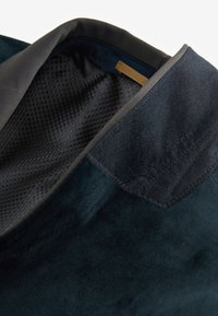 Borsa in camoscio blu scuro con una texture liscia, dotata di una fodera in rete e un dettaglio dorato all'interno. I bordi sono cuciti con cura.