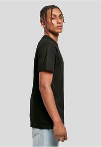 Black cotton t-shirt with short sleeves, round neckline, and a relaxed fit, paired with light blue denim jeans. Plain design, no patterns or accents.