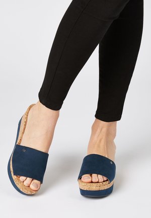 Marineblauwe slipper sandalen met een kurken sleehak zool, voorzien van soepele suède banden en een open teen ontwerp voor comfort en stijl.