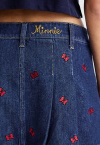 Džínsové šortky so vzormi červených vyšité motýľov, zlatým logom "Minnie" na páse a klasickým dizajnom s piatimi vreckami.