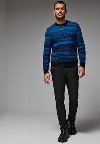 Blå och svart randig tröja med rund halsringning, kombinerad med svarta byxor och svarta snörskor, mot en neutral bakgrund.