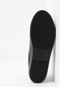 Black athletic shoe shown from a side angle, featuring a textured upper, smooth sides, and a patterned rubber sole with visible size label.