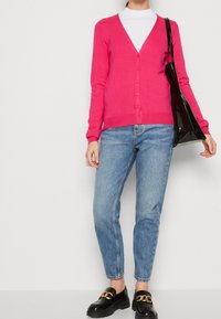 Fuchsia V-ringad cardigan med knäppning, i kombination med ljusblå raka jeans och svarta loafers med guldkedjedetalj.