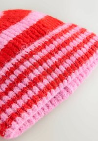 Knit beanie in red and pink, featuring horizontal stripes. Textured wool with a soft, fuzzy appearance, showcasing alternating color patterns.