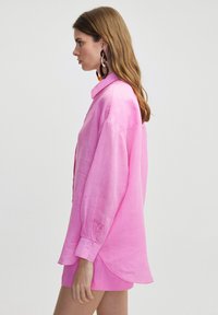 Blusa de lino rosa con un corte relajado, mangas largas y puños abotonados. Con dobladillos redondeados notables y una textura ligera para mayor comodidad.