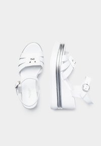 Sandalias de plataforma blancas con diseño de correas, acentos plateados, cierre de hebilla y suela texturizada. Ideales para uso casual.