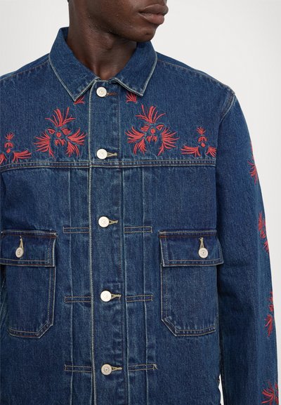 Denim jacket featuring red floral embroidery across the shoulders, front button closure, two chest pockets, and contrasting stitching details.