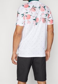 Krátký rukáv, bílá polo tričko s růžovým ovocem a květinovým vzorem, malými zelenými puntíky a tyrkysovým límečkem. Nosit s tmavými šortkami.