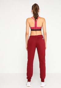 Pantalones de chándal burdeos con puños elásticos y cintura con cordón, combinados con un sujetador deportivo negro y rosa con diseño de espalda de nadador.