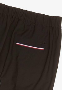 Czarne spodnie z elastycznym pasem, z kieszenią wpuszczaną i akcentami w czerwono-biało-niebieskie paski oraz wyszytymi inicjałami "T.H."