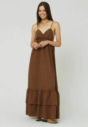 Robe maxi marron avec des bretelles fines, une taille froncée et un ourlet en volants superposés. Tissu lisse avec une finition mate, assorti à des bottes marron clair.