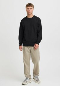 Suéter negro de punto con cuello redondo, puños y dobladillo acanalados; combinado con pantalones sueltos de color beige claro y zapatillas grises.