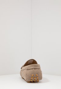 Beige suede moccasin, rounded back with contrast stitching, rubber sole with rounded nubs for grip, and a soft, textured finish.