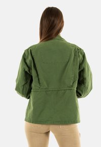 Chaqueta de algodón verde con un corte relajado, que presenta un cuello simple, detalle de bolsillo trasero y cintura elástica para un ajuste ajustable.