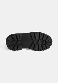 Zwarte rubberen loopzool met een uitgesproken profiel, voorzien van diepe groeven en hoekige noppen voor verbeterde grip en tractie.