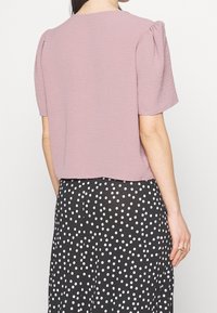 Top a maniche corte di colore rosa chiaro con finitura testurizzata e dettagli arricciati sulle spalle, abbinato a una gonna nera con pois bianchi.