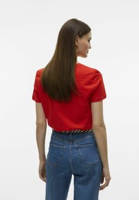 T-shirt en coton rouge à manches courtes, avec une coupe décontractée, associé à un jean en denim taille haute légèrement délavé et avec des poches arrière.