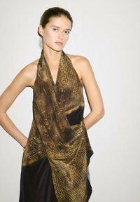 Robe brune et noire avec un tissu texturé et à motifs ; design halter ; drapés fluides ; éclat subtil ; silhouette moderne.