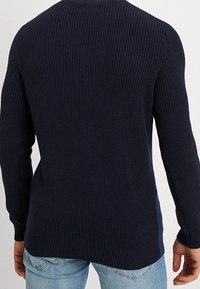 Pullover in maglina blu navy con texture a coste, maniche lunghe, scollatura rotonda e orlo posteriore leggermente più lungo. Finitura alla moda.