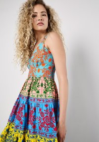 Robe colorée avec un motif floral et d'ananas en bleu, orange, vert, rose et jaune. Dotée d'un corsage ajusté et d'une jupe évasée.