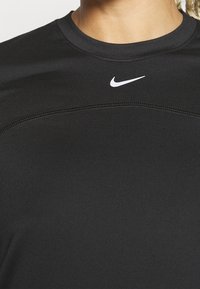 Černé sportovní tričko vyrobené z hladké, elastické látky. Má kulatý výstřih a bílou Nike logo umístěné ve středu hrudi.