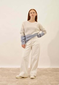Gebreide trui in crèmekleur met lichtblauwe zoom, gecombineerd met hoge witte broeken. Textuurmateriaal en ontspannen pasvorm.