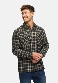 Sort og gulternet flannel skjorte med to brystlommer, knaplukning foran og lange ærmer, båret med blå jeans. Blødt, struktureret stof.