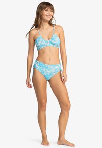 Blå blomster-bikini-sett med en cropped topp med tynne stropper og høy midje-bukser med sidesnøring. Jevnt, lett stoff.